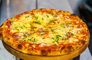 Fresh pizza on wooden stand on the table. Tasty pizza with tomato and cheese on the wooden background. Close-up