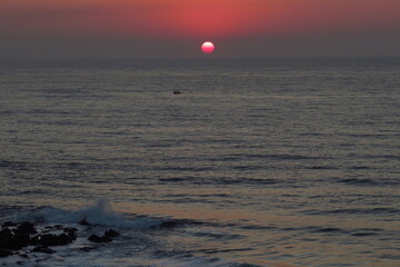 Sunrise over ocean with birds over sun and boat in foreground