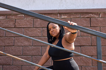 Beautiful afro american woman in black sportive clothes having rest on stairs, after exercises...