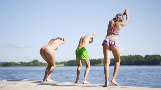 Happy family have vacations at the lake. Mother with daughter and son jump from the pier together. Boy and girl diving from the dock into the water. Children having fun.