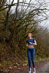 Full-lenght portrait of confident focused caucasian athlete female running in forest, dressed in blue stylish fashionable sportive clothes, outdoors on fresh air, cold weather, in the morning