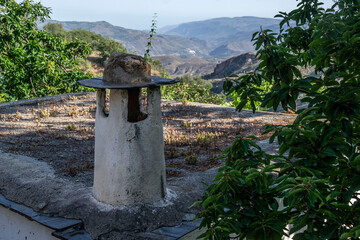 Typical white chimney of the Alpujarra on a roof with mountains in the background in Laroles de Nevada with green leaves