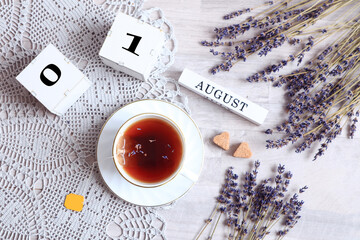 Calendar for August 1 :the name of the month of August in English, cubes with the number 01, a cup of tea on a gray napkin, two pieces of sugar in the shape of a heart, lavender branches, top view