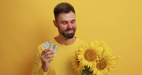 Pleased bearded man allergic to smell of sunflowers shows anti allergy medicine shows pills wears casual jumper smiles gladfully isolated over vivid yellow background. Immune system response