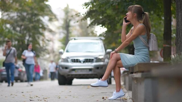 Young woman sitting on a bench talking on her mobile phone outdoors on city street in summer.