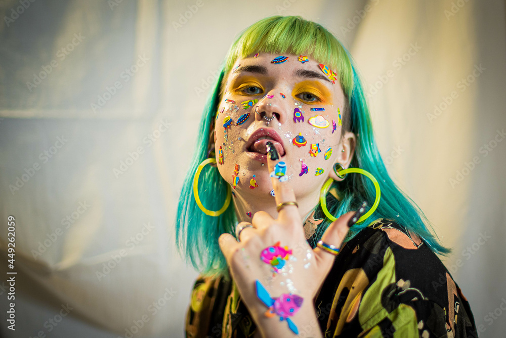 Wall mural Closeup fashion portrait young pretty beautiful girl with green and blue hair. Beautiful fashion girl with luxury professional makeup and funny emoji stickers glued on the face. Young woman