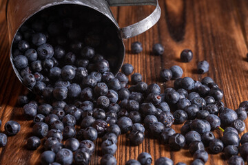 Fresh blueberries are pouring out of mug on a wooden background