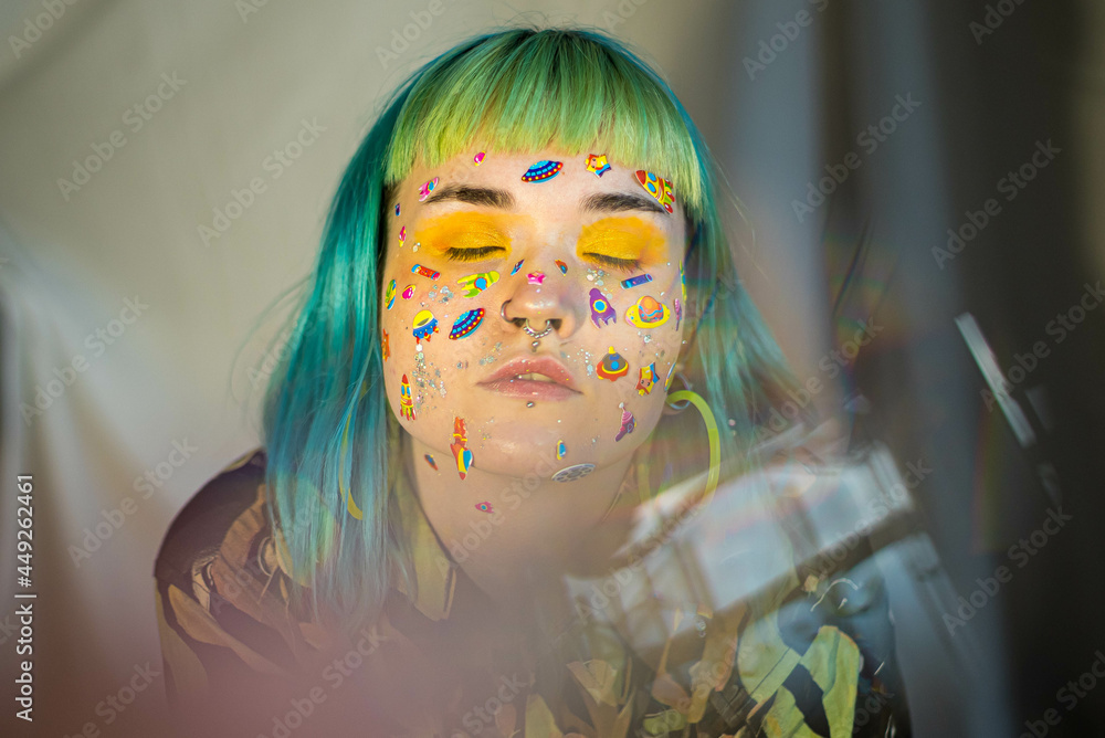 Wall mural Closeup fashion portrait young pretty beautiful girl with green and blue hair. Beautiful fashion girl with luxury professional makeup and funny emoji stickers glued on the face. Young woman