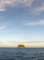 Vertical shot of a small island in the sea with a beautiful sky view © Mark Kucharski/Wirestock