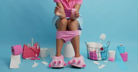 Unrecognizable woman holds cotton tampon and menstruation cup chooses best product wears domestic slippers pants pulled down on legs being in lavatory rooom against blue background. Hygiene.