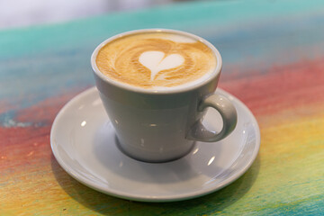  taza caliente del café con leche del capuchino con el arte del latte en forma de corazón en la mesa de madera colorida en el concepto de café, comida y bebida.