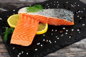 Two fresh raw salmon fillets with dill herb garnish and lemon slices on a slate serving board