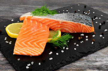 Two fresh raw salmon fillets with dill herb garnish and lemon slices on a slate serving board