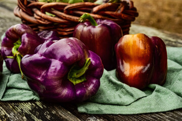 whole fresh purple bell peppers in food still life on rustic wood tabletop with green cloth and wicker basket