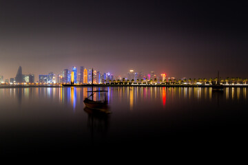 Fototapeta premium Illuminated skyline of Doha at night with traditional wooden boat in the foreground, Qatar, Middle East.