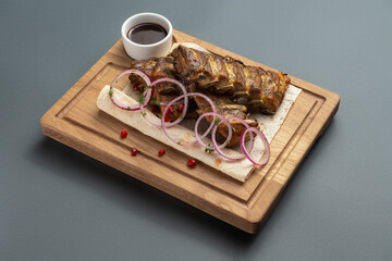 shashlik or grilled meat ribs with sauce and onion on pita on wooden board