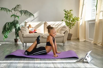 Tuinposter Kid repeating exercises while watching online yoga gymnastics session © Inna Vlasova
