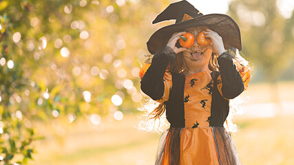 Little witch girl indulges and has fun with two little pumpkins on Halloween.
