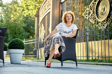 Woman 50 years sitting in chair near sidewalk cafe.