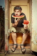 Man sitting on wooden toilet latrine and eating watermelon
