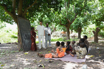 Tall white volunteer teaching a group of children in an open air summer camp in a remote village in...