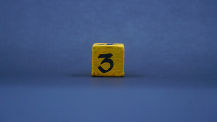 Wooden block with number 3. Yellow color on dark background