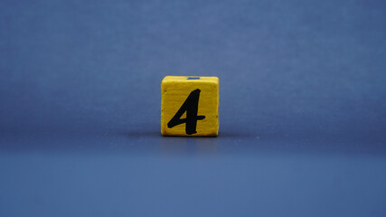 Wooden block with number 4. Yellow color on dark background