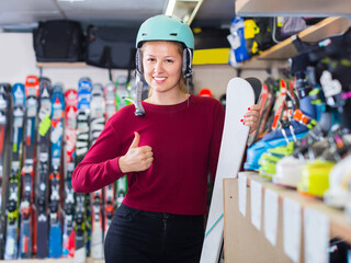 Portrait of client girl in helmet who is standing with ski in sport shop.