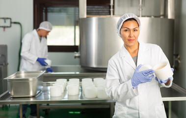 Portrait of skilled Asian woman wearing white uniform working in shaping workshop of cheese dairy..