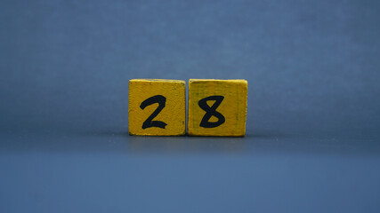 Wooden block with number 28. Yellow color on dark background