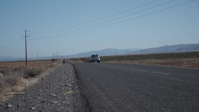 Low Angle View Of Car Driving Away. Power Lines Leading Across Road In Dry And Dusty Landscape In Countryside. Morocco, Africa