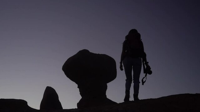 Silhouette of Female Hiker With Backpack and Photo Camera Hiking Up on Hill With Strange Rock Formation, Slow Motion Full Frame