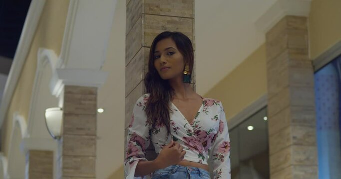 A sexy young fashion model standing in a mall with overhead lights in the background