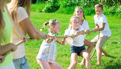 Glad kids with parents playing tug of war during joint outdoors games on sunny day