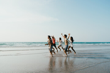 Group of friends running having fun on the white sand beach amid the blue sky. Concept of Summer,...