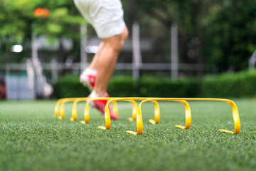 A yellow step-over ladder for speed and leg strength training equipment (Focus), Photo with action of a sport player is training on it as blurred background. Sport object and action photo.