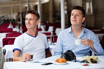 Fototapeta na wymiar Positive couple of male tourists talking and drinking coffee