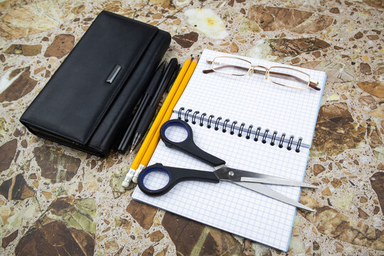 Office, business or workstation still life with purse and spectacles alongside an open notebook with pencils and scissors over a marble counter viewed high angle