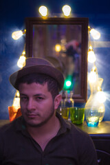 portrait of a serious looking young adult man wearing a hat with a mirror cabinet and lights behind...