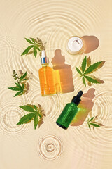 CBD oil cosmetics in jar and bottle with dropper, cannabis leaves on transparent oily background...