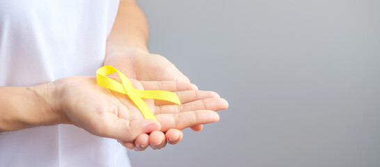 hand holding Yellow Ribbon for supporting people living and illness. September Suicide prevention day, Childhood, Sarcoma and bone cancer awareness month concept