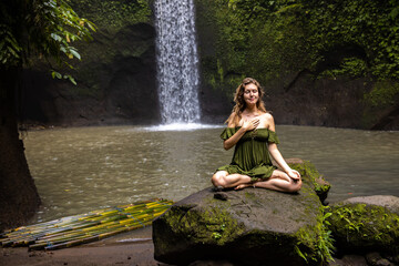 Yoga lotus pose. Caucasian woman sitting on the stone, meditating, practicing yoga and pranayama. Breathing exercise. Closed eyes. Hand in gyan mudra. Yoga retreat. Tibumana waterfall, Bali