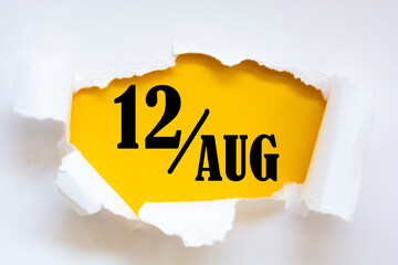 august 12. 12th day of the month, calendar date. Hole in paper with edges torn off. Yellow background is visible through ragged hole. Summer month, day of the year concept.