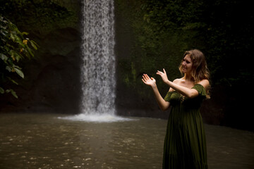 Portrait of Caucasian woman near the waterfall. Enjoy nature. Water splash. Young woman wearing green dress. Travel to Asia. Copy space. Tibumana waterfall, Bali