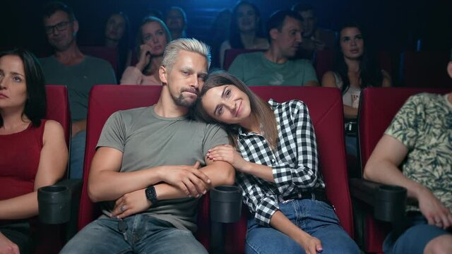 Happy couple hugging at movie theater sitting on armchair in row spectators enjoying romantic date