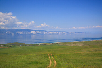 A bright summer landscape. A hilly shore of the Lake Baikal. A green meadow under a blue sky. A...