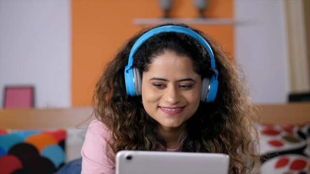 Portrait of a pretty Indian lady watching a movie on a tablet - Online movie  OTT . Young female with black hair relaxing alone at home - modern lifestyle. Video chat  Video call