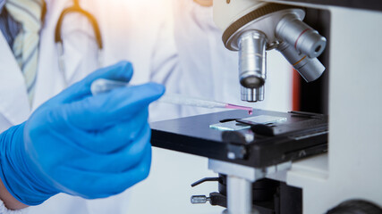medical or scientific researcher researching and experimenting Multi-colored solution, vial and microscope In the laboratory or in the laboratory by wearing blue gloves and white clothing completely.