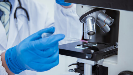 medical or scientific researcher researching and experimenting Multi-colored solution, vial and microscope In the laboratory or in the laboratory by wearing blue gloves and white clothing completely.