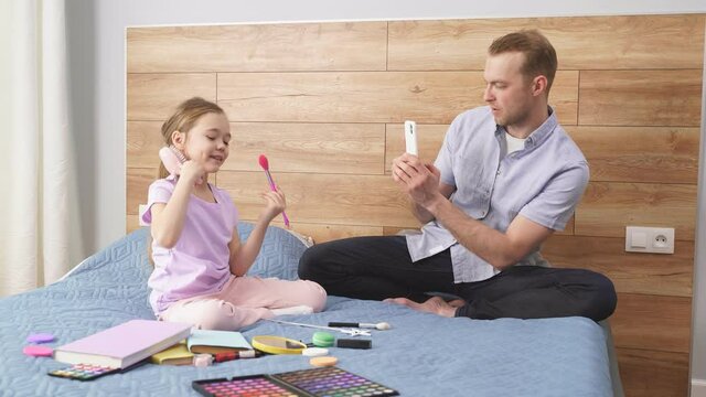 little girl show new cosmetics at phone's camera in hands of her father, young caucasian man take photo, enjoy spending time with daughter.